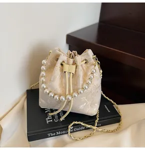 Detail of embroidered butterfly pattern on a beige silk bucket bag with pearl handle