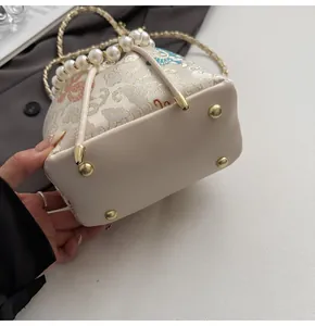 Detail of embroidered bucket bag featuring pearl handle and golden protective metal feet