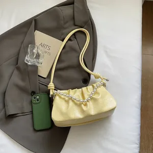 Detail of creamy yellow ruched underarm bag with elegant pearl chain and knotted strap