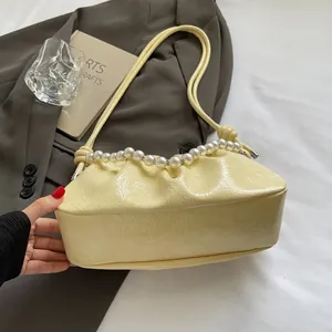 Detail of light yellow ruched cloud bag with glossy finish and elegant pearl handle