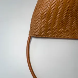Detail of caramel woven leather texture and smooth rounded handle on a bucket bag