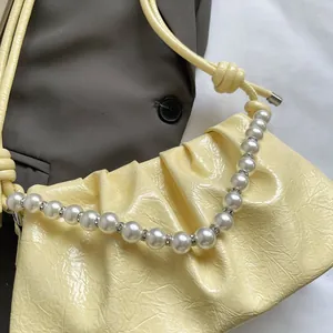 Detail of light yellow ruched patent leather bag with pearl handle on grey blazer