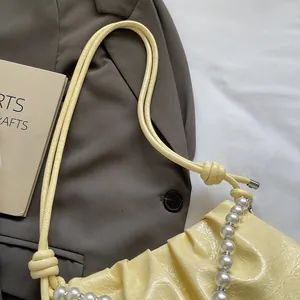 Close-up of yellow pleated shoulder bag with white pearl chain and glossy finish