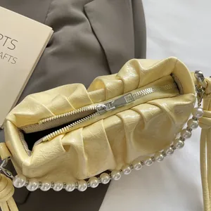 Close-up of pleated yellow cloud bag featuring glossy finish and elegant pearl chain strap