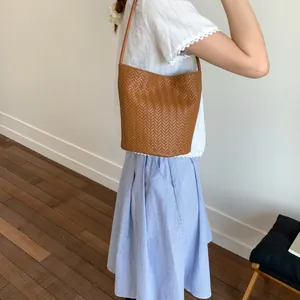 Detailed close-up of brown woven bucket bag texture with thin leather shoulder strap