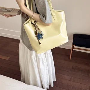 Detail of a creamy yellow glossy leather tote bag with star charms worn over the shoulder