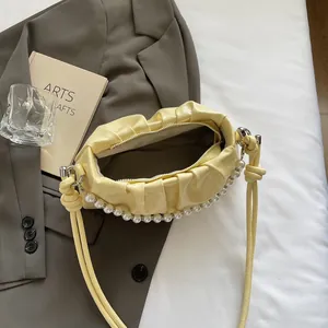 Detailed view of yellow ruched handbag with elegant pearl trim and sleek zip closure