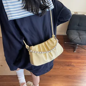 Detail of light yellow ruched underarm bag with decorative pearl chain and shoulder strap