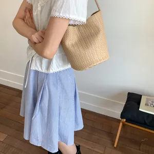 Detail of light brown woven bucket bag with herringbone texture and slim shoulder strap