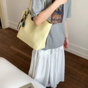 Close-up of light yellow tote bag featuring a leather knot and blue fish charm detail