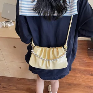 Detail of pale yellow pleated bag with white pearl chain and textured leather surface