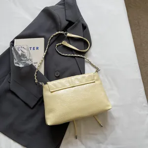 Detailansicht der glänzenden beigen Umhängetasche mit Kette auf grauem Sakko