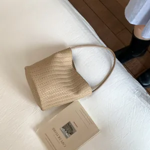 Close-up of khaki woven bucket bag with herringbone texture on a white cloth background
