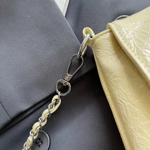 Detail von cremegelbem Leder mit Faltenstruktur, silbernem Haken und Kettenriemen