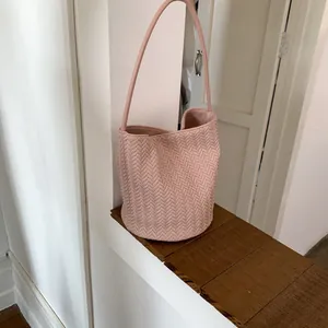 Macro detail of pink woven leather bucket bag with elegant V-pattern texture and long strap