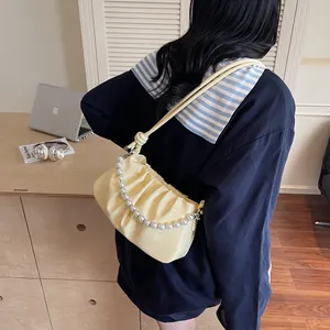Detail of yellow pleated shoulder bag with pearl handle and wave texture finish