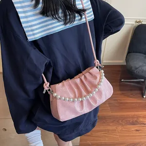 Detail of pink pleated crossbody bag with glossy finish and white pearl handle