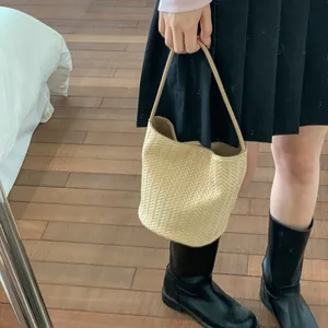 Close-up of beige herringbone weave texture on a bucket bag styled with a pleated skirt