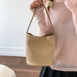 Chic beige woven bucket bag shown on shoulder with minimalist strap and summer outfit