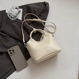 Dettaglio borsa a mano in pelle beige testurizzata con logo inciso e manico tondo