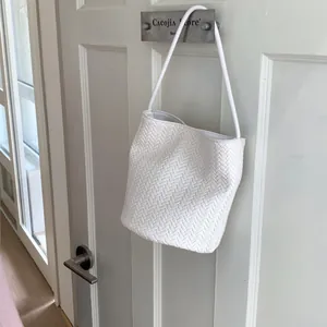 Close-up of white woven bucket bag with herringbone texture hanging on a metal hook