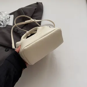 Dettaglio macro della borsa in pelle testurizzata bianco crema con logo a rilievo e cuciture