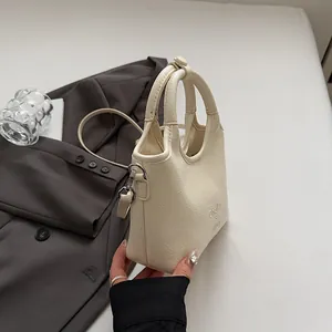 Dettaglio borsa color crema in pelle a pieghe con manico rotondo e dettagli in metallo