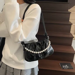 Detail of black pleated patent leather shoulder bag with elegant white pearl chain
