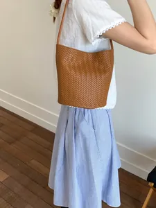 Brown woven bucket bag with shoulder strap shown on model for a trendy summer look