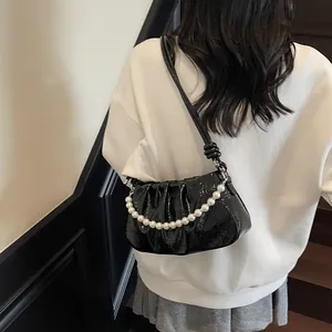 Detail of black pleated shoulder bag featuring glossy patent leather and a pearl chain
