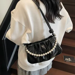 Detail of black pleated shoulder bag with pearl chain handle and glossy leather finish