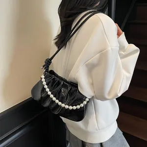 Detail of black pleated cloud bag with glossy finish and decorative pearl chain strap
