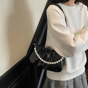 Detail of black pleated cloud bag with elegant large pearl chain and glossy finish