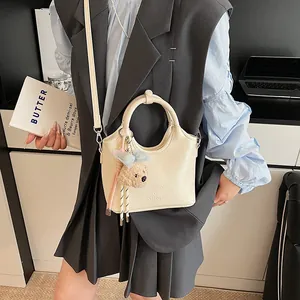 Dettaglio di mini borsa crema con trama a rilievo e ciondolo a forma di orsetto