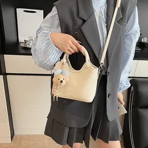 Primo piano della borsa in pelle color crema con trama litchi e pendente a orso