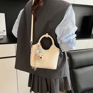 Dettaglio borsa in pelle crema con marchio a rilievo e ciondolo a forma di orsetto