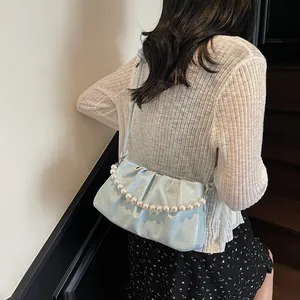 Detail of light blue pleated hobo bag with glossy finish and elegant pearl handle
