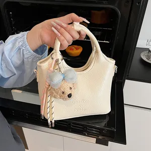 Dettaglio borsa in pelle crema con logo del marchio e ciondolo orsetto a fiocco blu