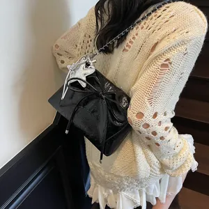 Detailaufnahme einer schwarzen glänzenden Schleifentasche mit Sternanhänger am Model