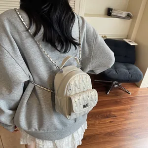 Close-up of white mini backpack with V-quilt pattern, sparkling rhinestones and chain strap