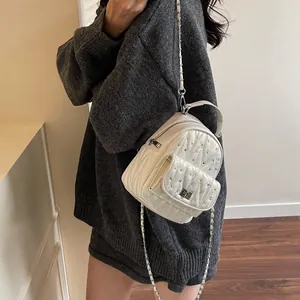 Close-up of a mini cream-white quilted backpack with sparkling rhinestones and chain strap