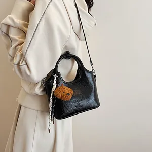 Dettaglio borsa in pelle verniciata nera con ciondolo a cucciolo e logo del marchio