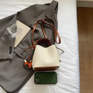 Detail of cream woven bucket bag with brown leather trim and horse charm on a blazer