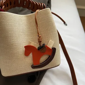Detail of a beige textured bucket bag with woven leather handle and horse charm