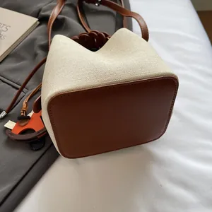 Detail of beige canvas bucket bag with brown leather base and orange pony charm