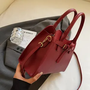 Gros plan du sac en cuir bordeaux montrant les boucles dorées et les coutures précises