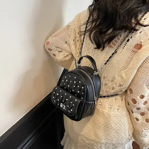 Detail of a mini black quilted backpack with silver studs and chain strap on a model