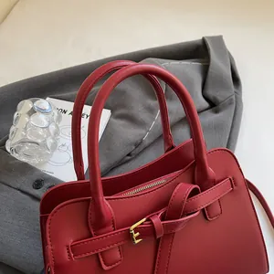 Détail d'un sac cabas rouge en cuir avec boucle en métal doré sur une veste grise