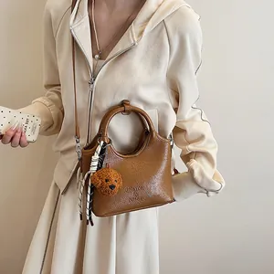 Dettaglio borsa a secchiello marrone con ciondolo a orsetto e accessorio foulard a righe