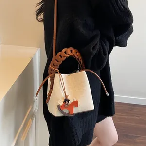 Detail of white canvas bucket bag with brown woven handle and orange horse charm